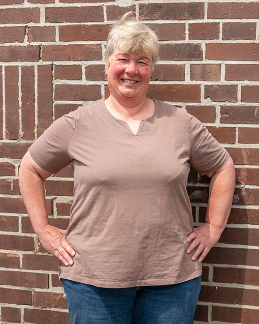 Die stolze Weiterbildungsteilnehmerin Astrid Estel steht, die Hände auf die Hüften gestützt, vor einer geziegelten Hauswand.