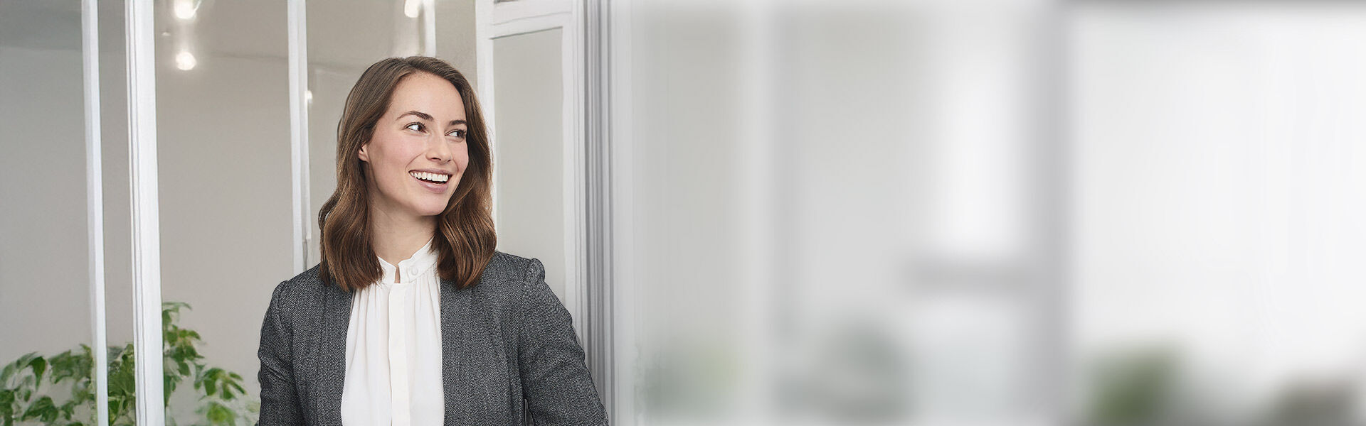 Seriös gekleidete Frau steht im Büro und lächelt